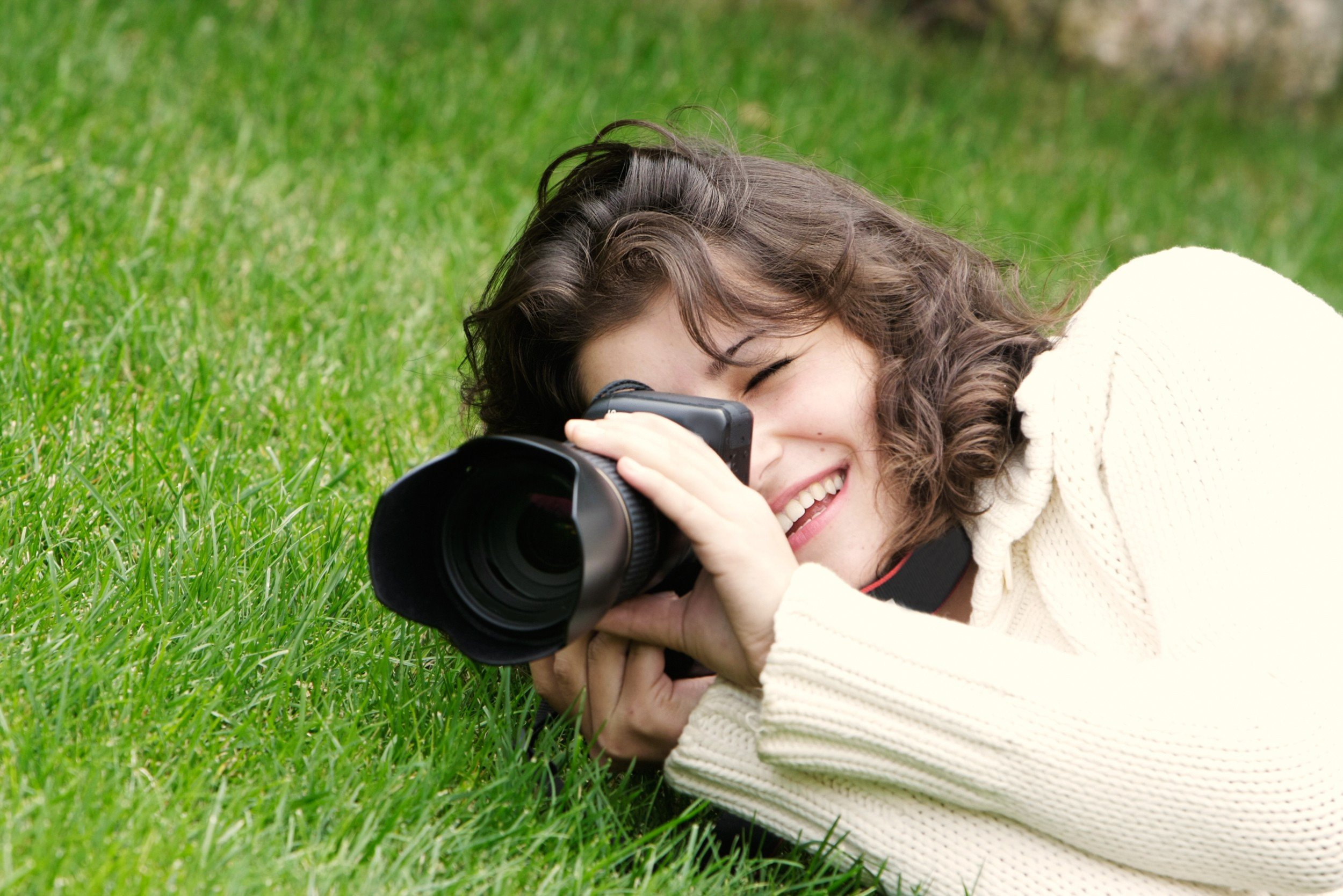 Young woman taking picture with dslr camera lying on green grass