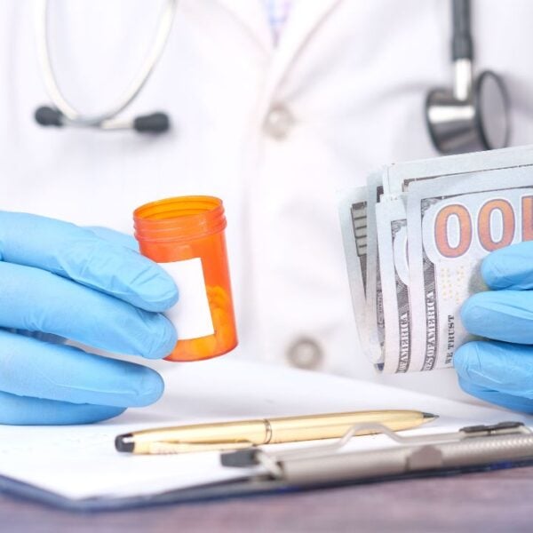 Doctor in gloves holding pill bottle and cash, highlighting medical expenses.