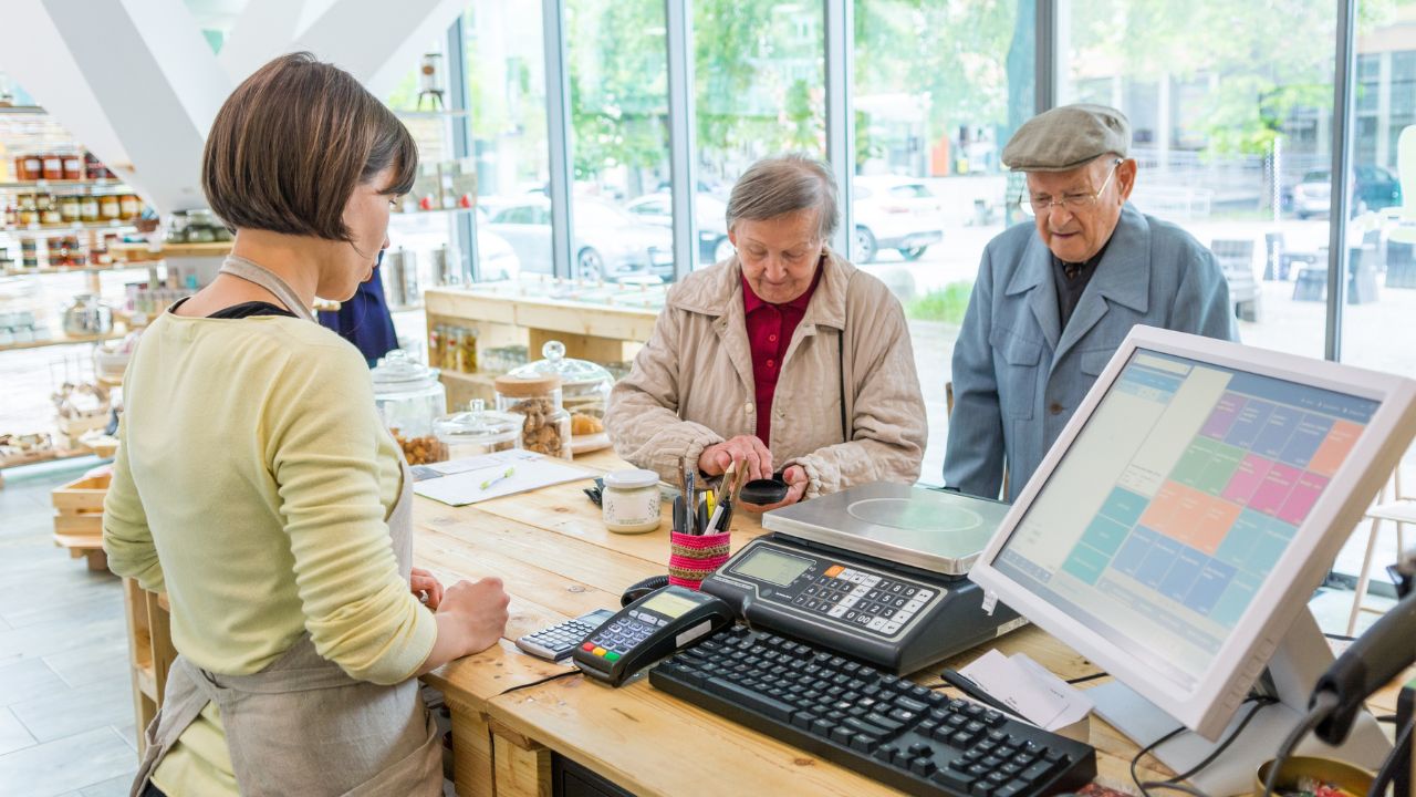 Elderly couple at cashier desk paying to teller in local zero waste store.