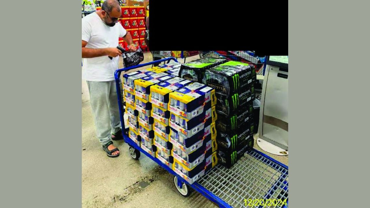 Investigative photograph showing a man beside a shopping cart stacked with cases of energy drinks at a retail store, with background shoppers redacted.
